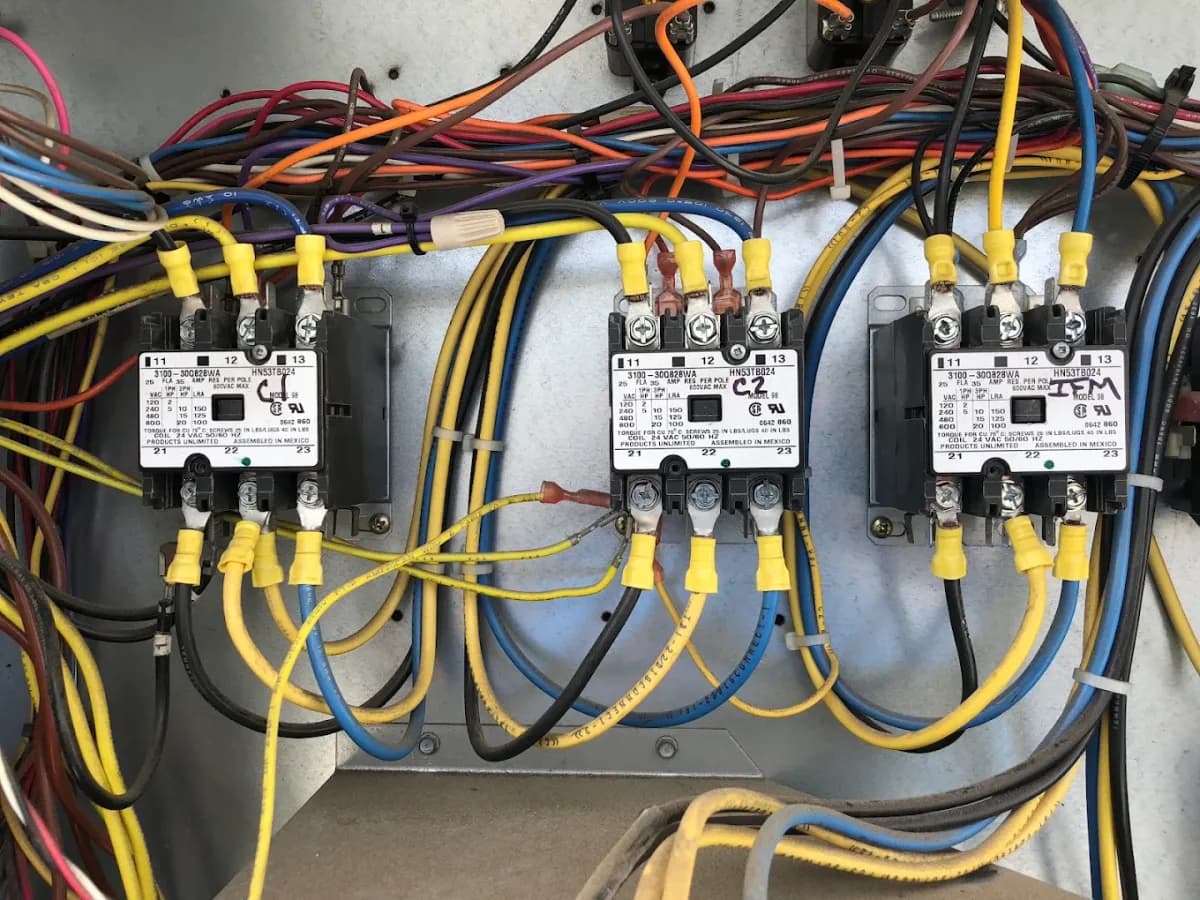 A bank of contactors and coloured control wiring inside an opened heating and cooling unit