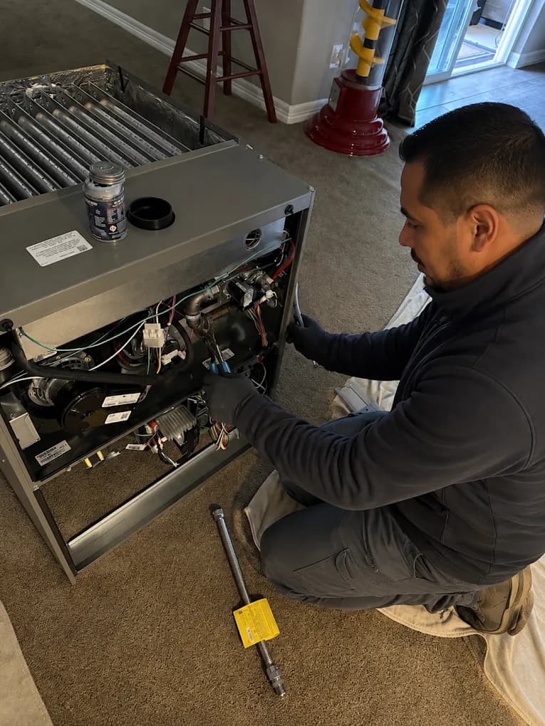 An ASAP Heating and Cooling technician working inside an open furnace cabinet in a home