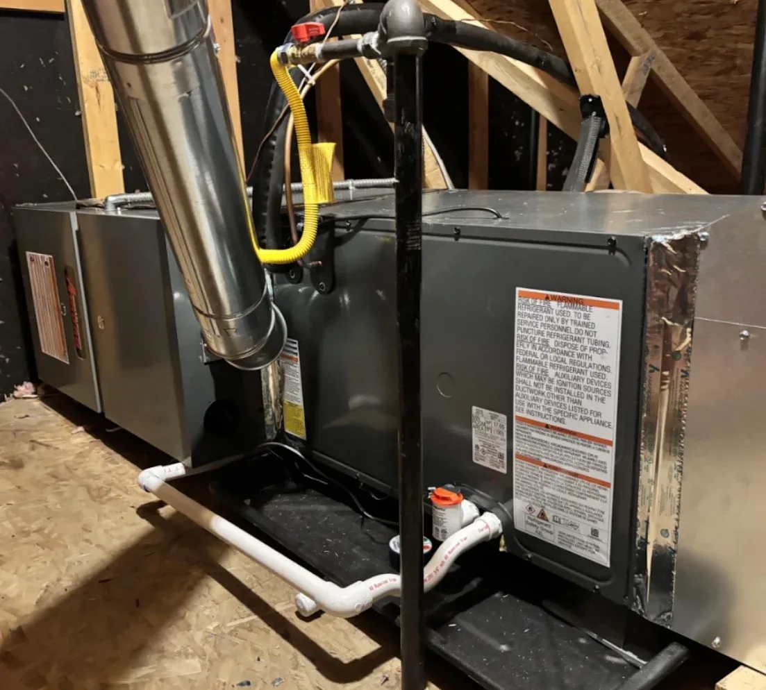 A gas furnace and evaporator coil installed side by side in an attic, each sitting on a drain pan with condensate lines run out to the front