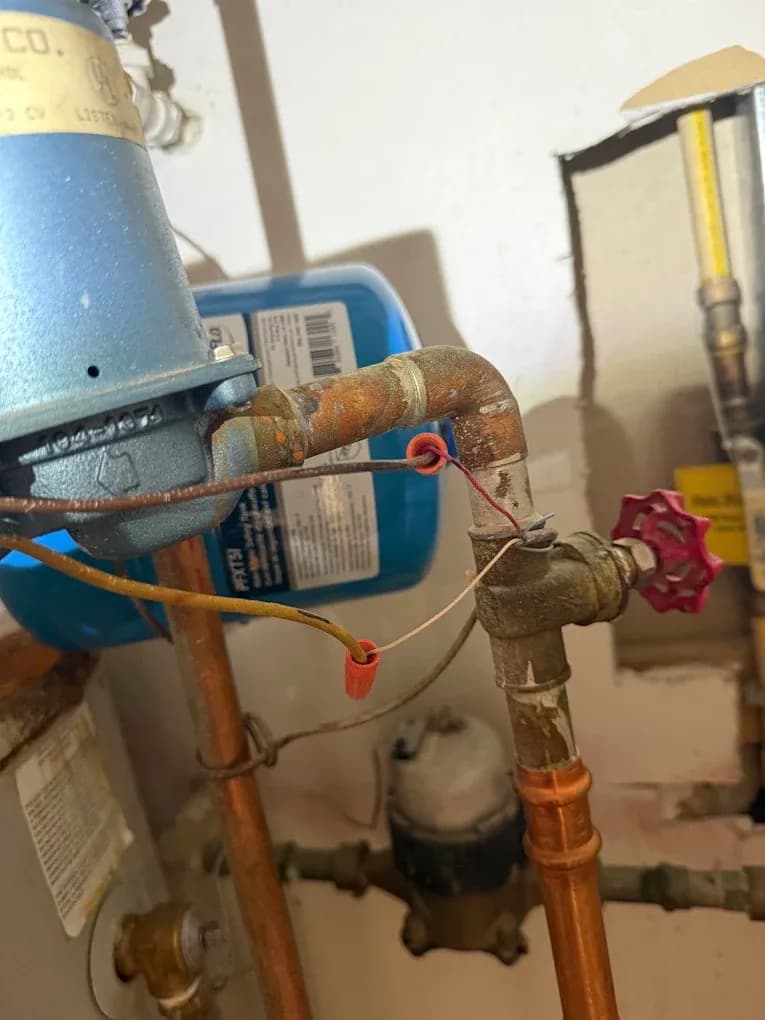 A boiler circulator pump and expansion tank on aged copper piping, photographed close up during a heating system repair