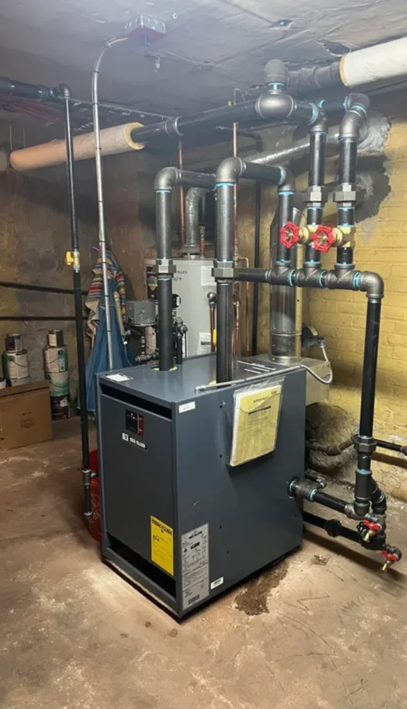 A newly installed cast iron boiler in a basement, piped in black steel with shut off valves and risers carried up to the main overhead