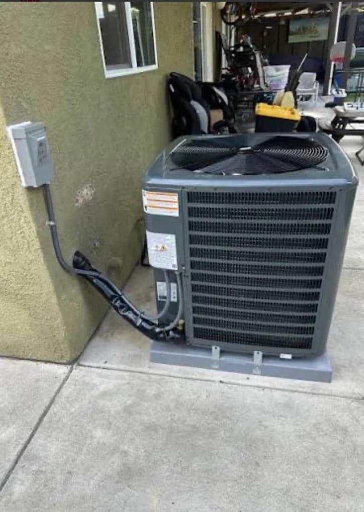 An outdoor air conditioning condenser standing on a pad beside the electrical disconnect box it is wired into