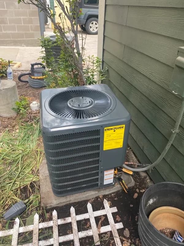 An outdoor air conditioning condenser on a pad at the side of a home, beside a planted bed