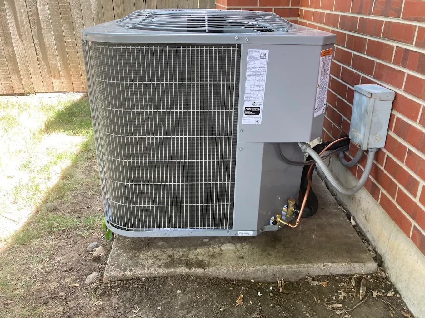 A newly installed outdoor air conditioning condenser on a concrete pad beside a home, wired into the electrical disconnect next to it