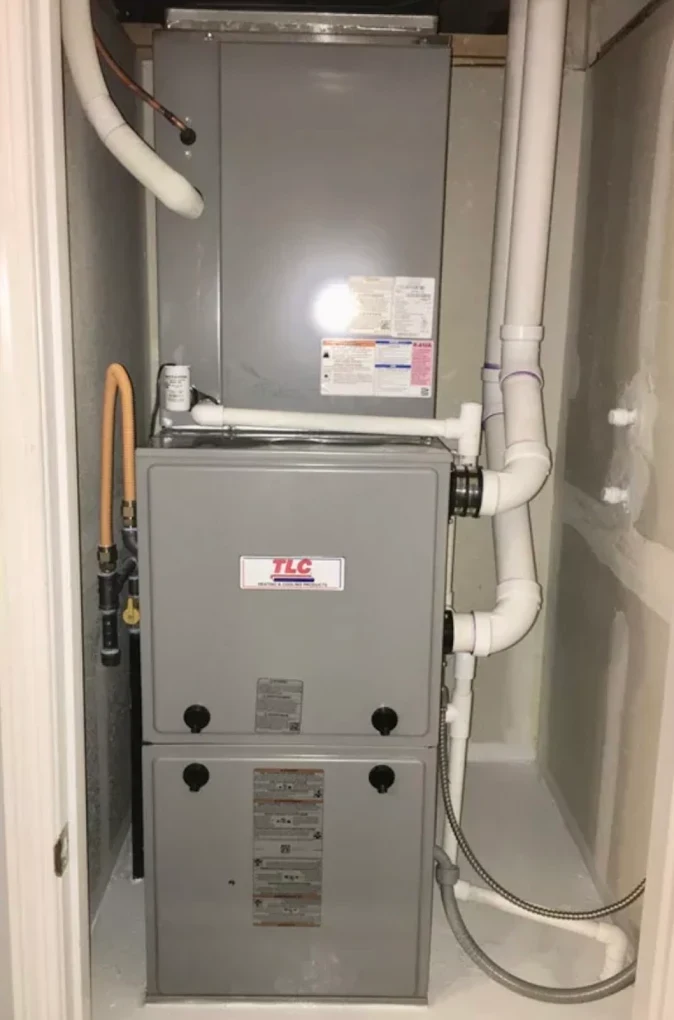 A residential gas furnace installed in a utility closet with its flue venting and condensate lines run overhead