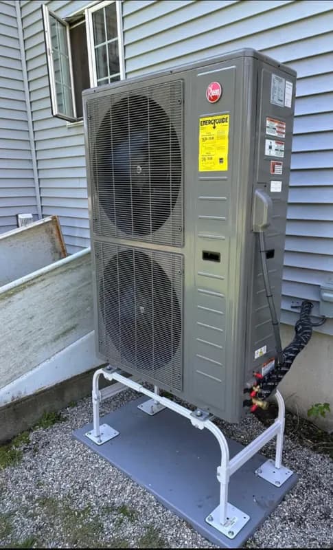 A newly installed two fan outdoor heat pump raised on a steel stand beside a home