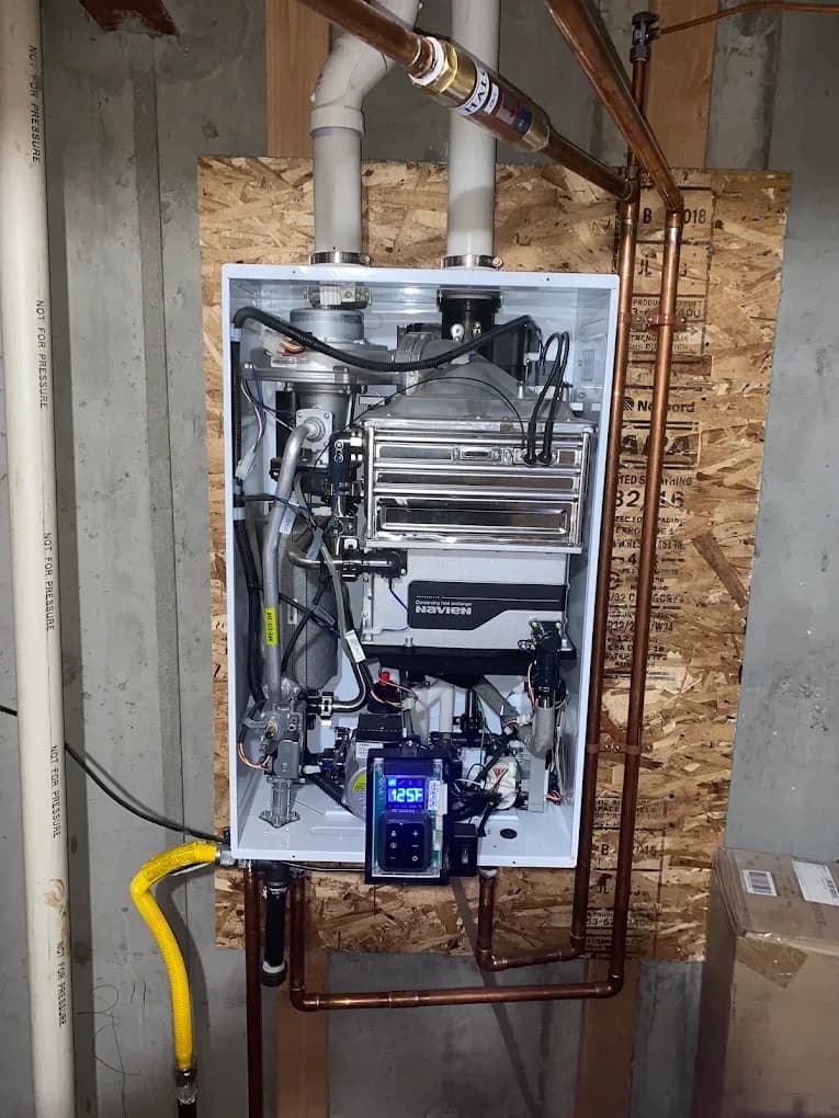 A wall-mounted tankless water heater opened for service, showing its condensing heat exchanger, gas train and digital temperature control