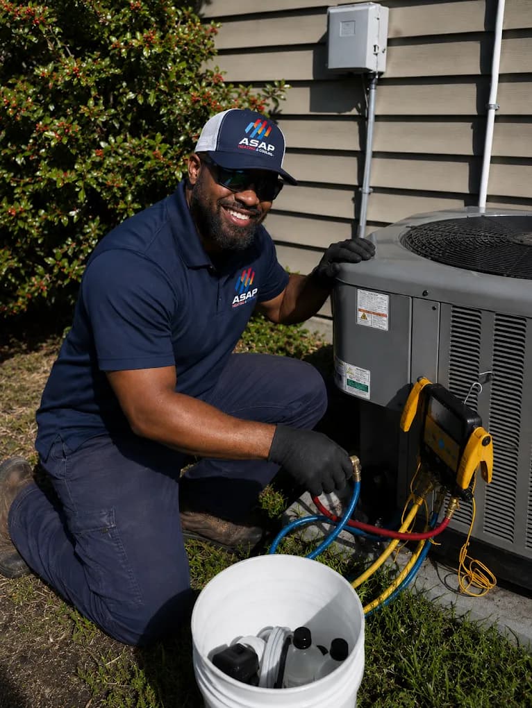 An ASAP Heating and Cooling technician kneeling beside an outdoor condenser during an air conditioning service call